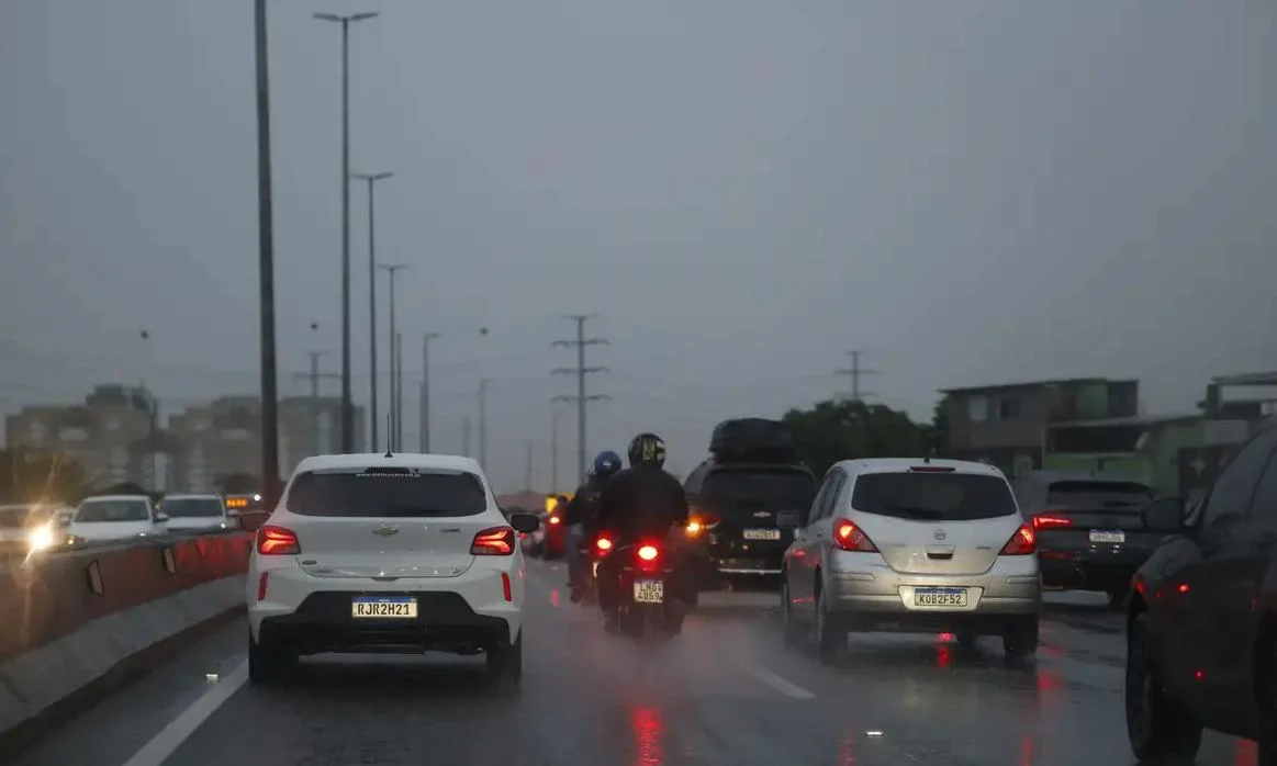 Rua movimentada em Belford Roxo sob chuva e céu nublado nesta segunda-feira